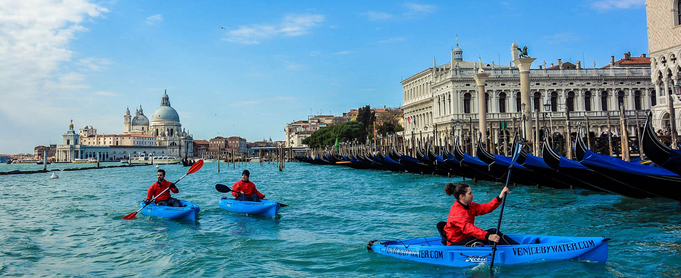Kayakers on calm open water in St Mark's basin with gondolas moored behind